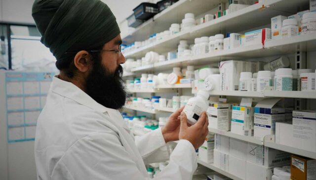 Pharmacist with turban organizing shelves in a pharmacy, focused on healthcare.